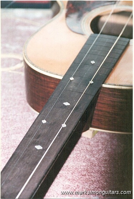 0040fbbig.jpg - A new fretboard is glued to the neck. Inlays are positioned with a drop of glue and aligned with the 2 strings shown. After the glue has set, A scribe is run around the inlays to create an outline, The inlays are then removed and a router is used to remove the bulk of wood where the inlays will recess into. The corners are removed with a sharp knife and chisel. The shell is then glued into the neck and sanded flush. The neck is not glued in at this point.